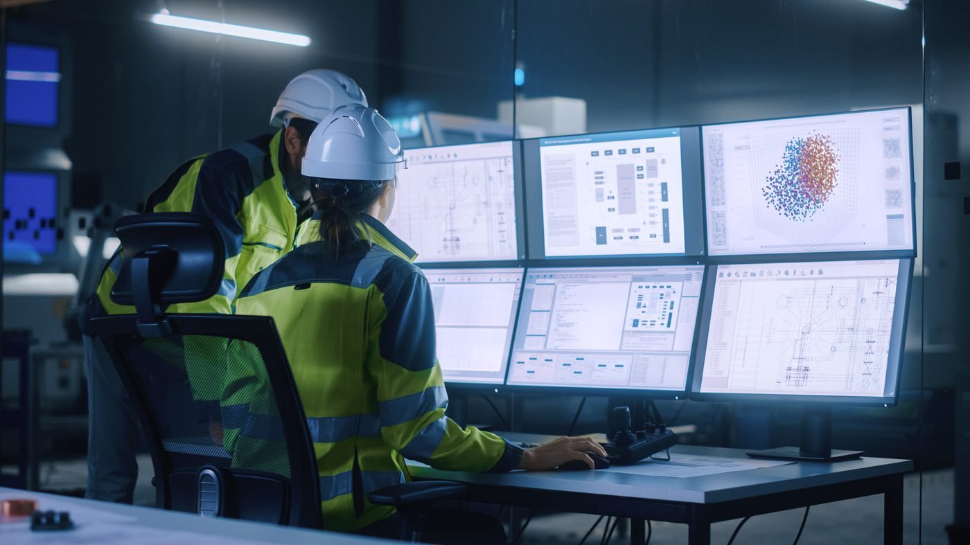 Engineers monitoring SCADA and control systems on a multi-screen wall in a control room